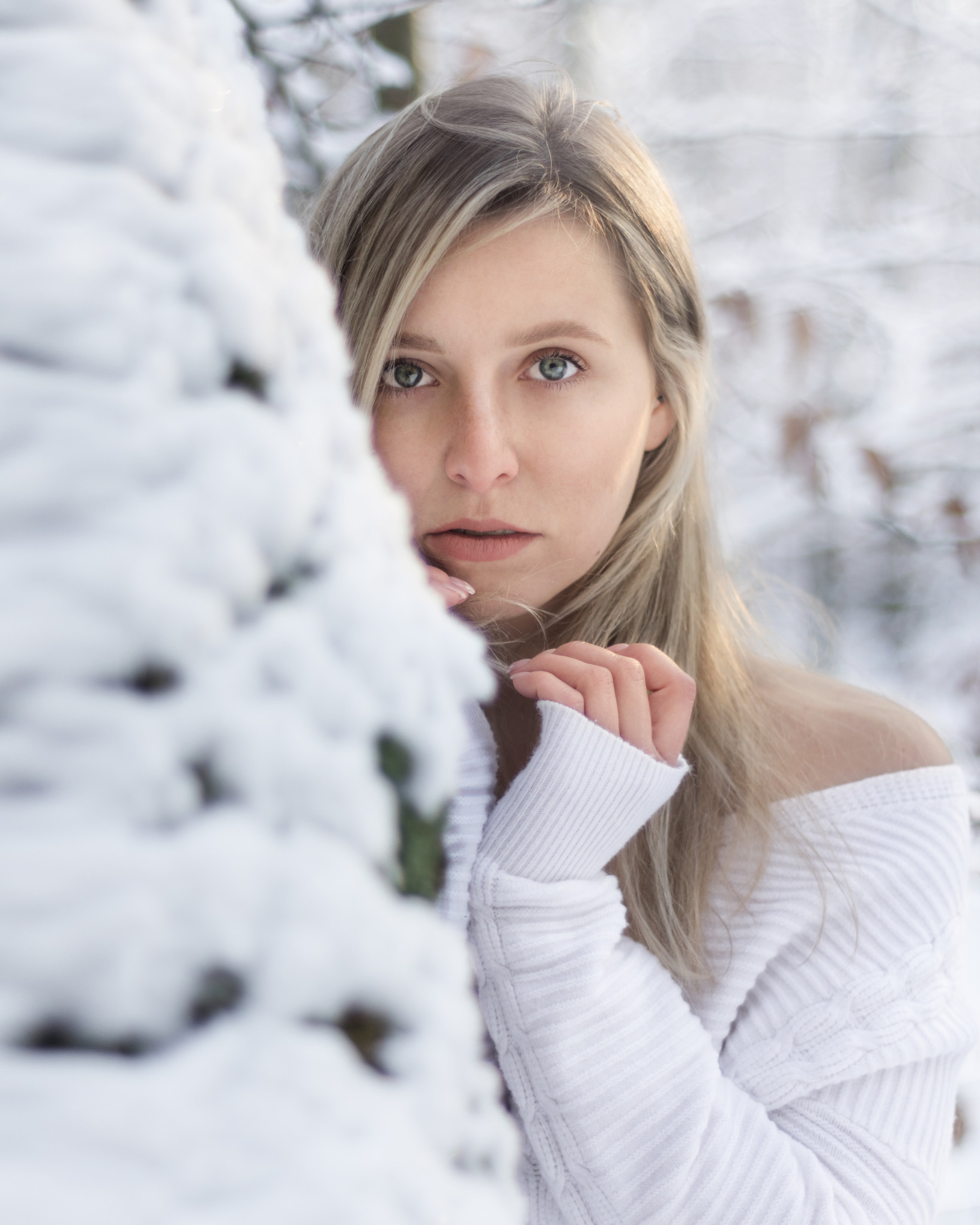 Kobiecy portret plenerowy w zimowej scenerii, jasny kadr z naturalnym ramowaniem przez gałęzie w śniegu